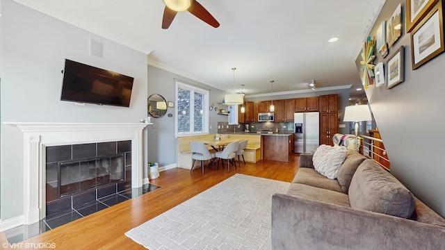 living area featuring ornamental molding, a ceiling fan, light wood-style flooring, and a tile fireplace
