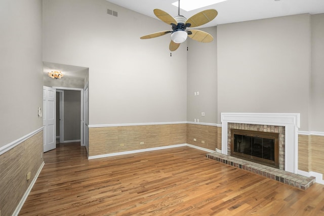 4240 Kingshill Cir, Naperville, IL 60564 - unfurnished living room featuring ceiling fan, wood finished floors, a brick fireplace, a high ceiling, and wainscoting