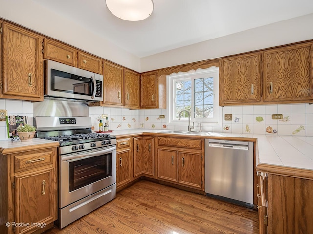 kitchen featuring a sink, appliances with stainless steel finishes, brown cabinetry, and backsplash