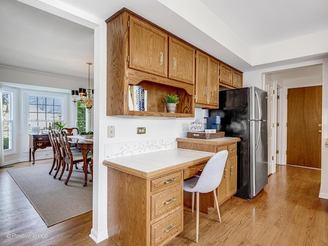 kitchen featuring open shelves, tile countertops, brown cabinets, light wood finished floors, and a notable chandelier
