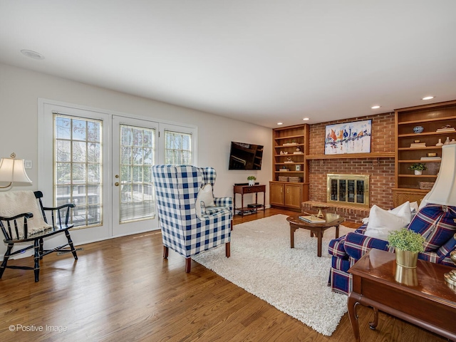 living area with a brick fireplace, built in shelves, french doors, recessed lighting, and wood finished floors