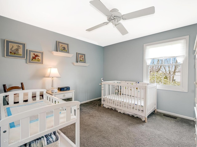 bedroom featuring ceiling fan, visible vents, a crib, baseboards, and carpet
