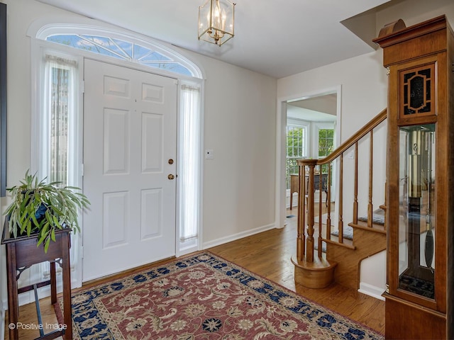 entryway featuring baseboards, stairs, wood finished floors, and a notable chandelier