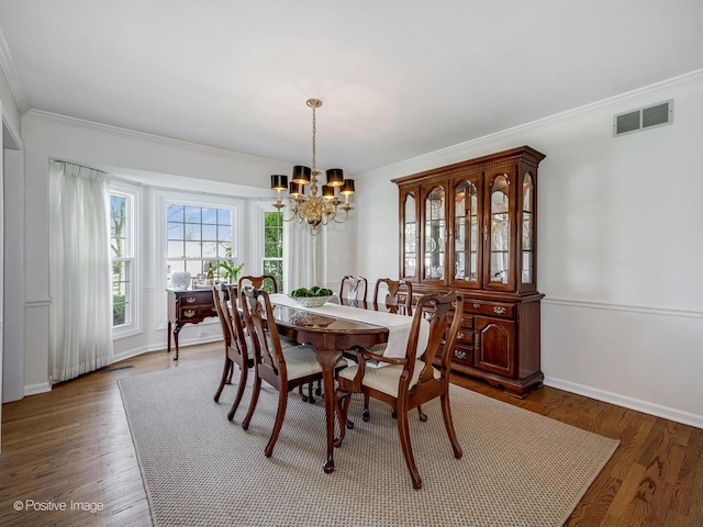 dining space featuring an inviting chandelier, crown molding, wood finished floors, and visible vents