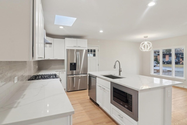kitchen with a sink, a skylight, stainless steel appliances, backsplash, and light stone countertops