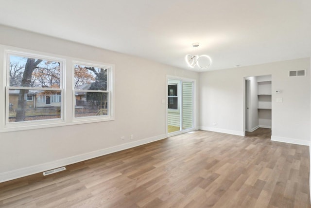 empty room featuring light wood finished floors, baseboards, visible vents, and an inviting chandelier