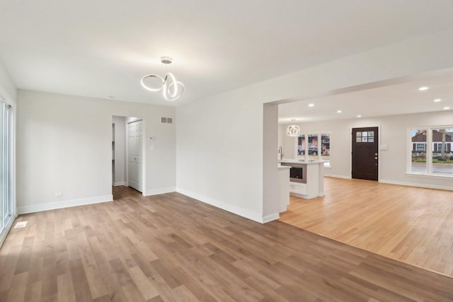 unfurnished living room featuring light wood-type flooring, baseboards, and a notable chandelier