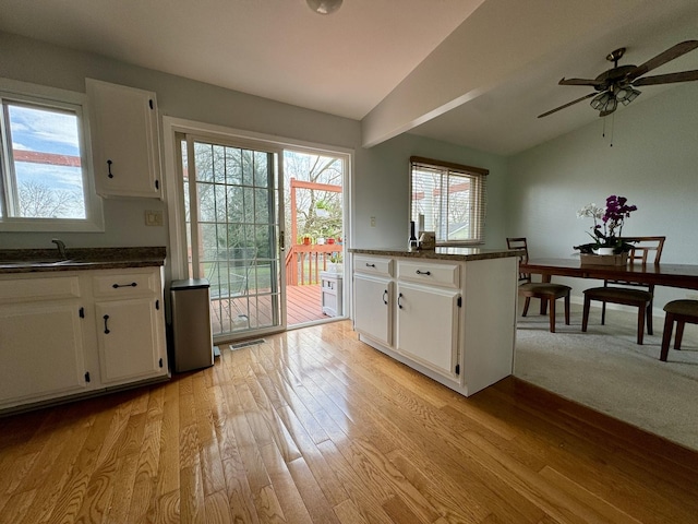 kitchen with lofted ceiling, white cabinets, dark countertops, ceiling fan, and light wood-type flooring