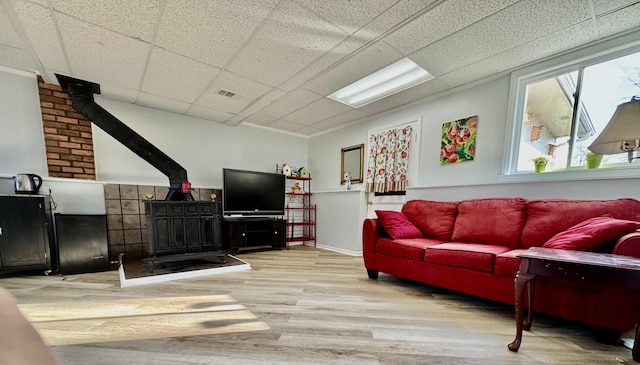living area featuring a wood stove, visible vents, a drop ceiling, and wood finished floors