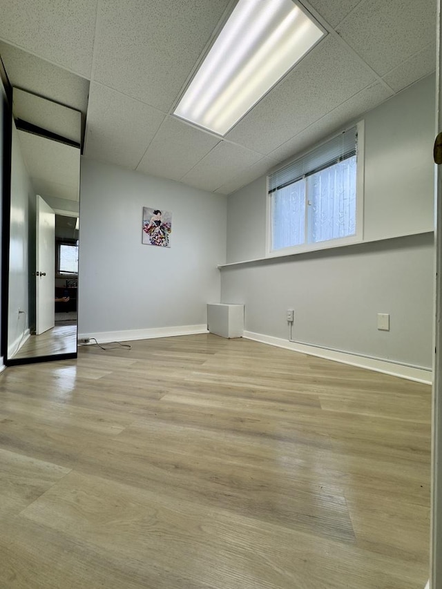 empty room featuring baseboards, wood finished floors, a wealth of natural light, and a drop ceiling