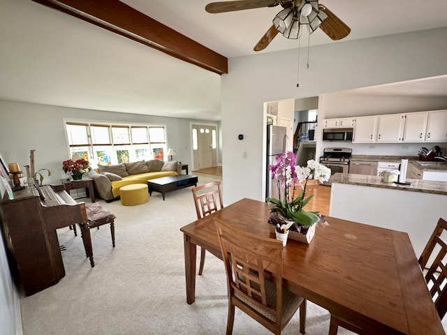 dining space featuring ceiling fan, vaulted ceiling with beams, and light carpet