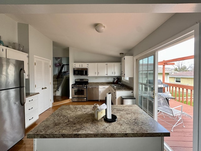 kitchen with a sink, vaulted ceiling, dark countertops, white cabinets, and appliances with stainless steel finishes