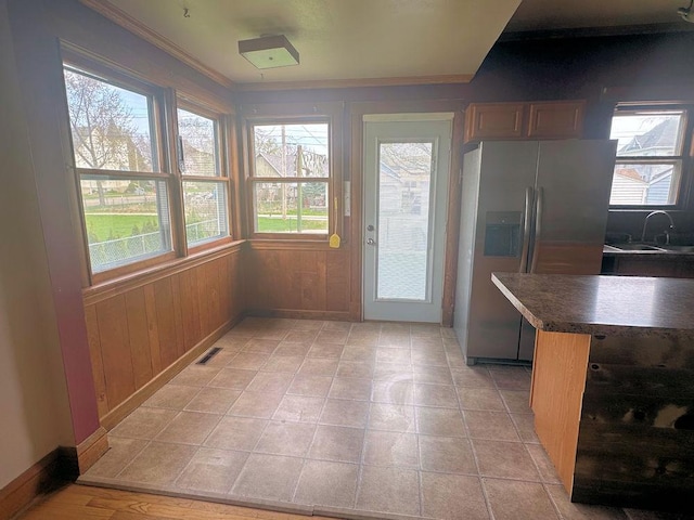 kitchen featuring crown molding, wood walls, a sink, stainless steel refrigerator with ice dispenser, and visible vents