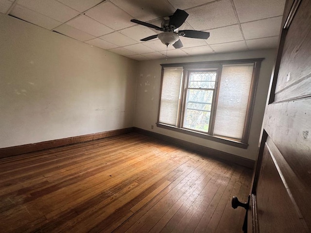 empty room with hardwood / wood-style floors, a drop ceiling, baseboards, and a ceiling fan