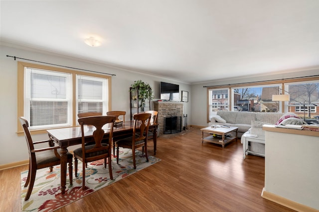 dining room with a fireplace, wood finished floors, baseboards, and ornamental molding