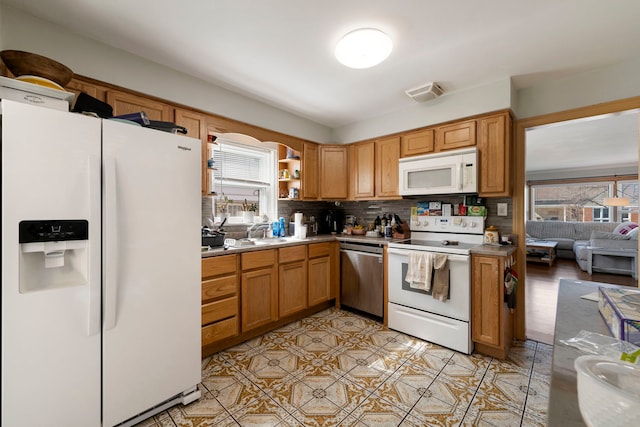 kitchen featuring a sink, brown cabinetry, white appliances, backsplash, and visible vents