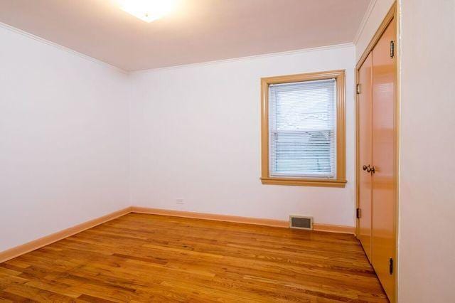 unfurnished room with wood finished floors, visible vents, crown molding, and baseboards