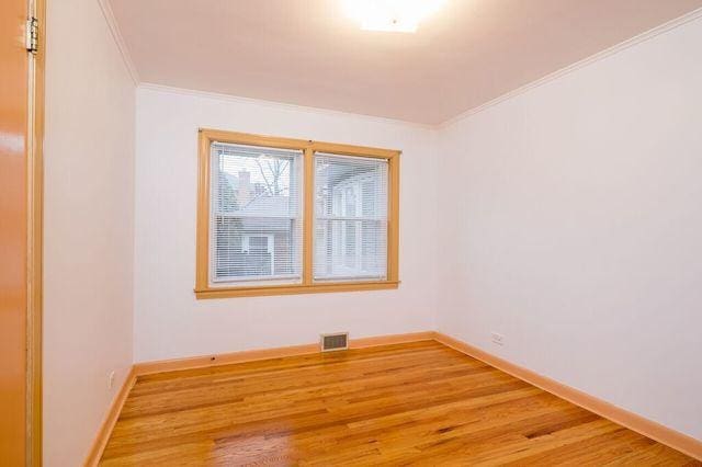 spare room with baseboards, ornamental molding, light wood-style floors, and visible vents