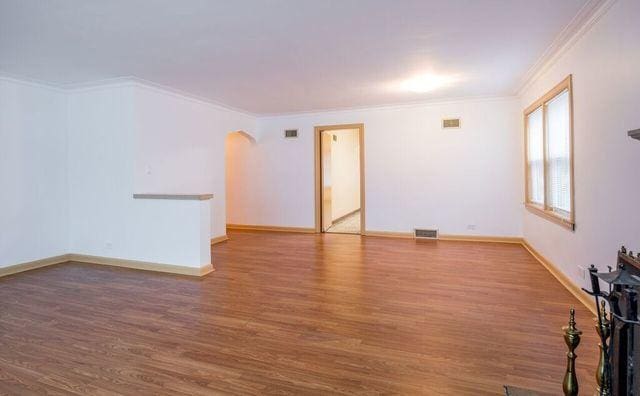 spare room featuring arched walkways, ornamental molding, wood finished floors, and visible vents