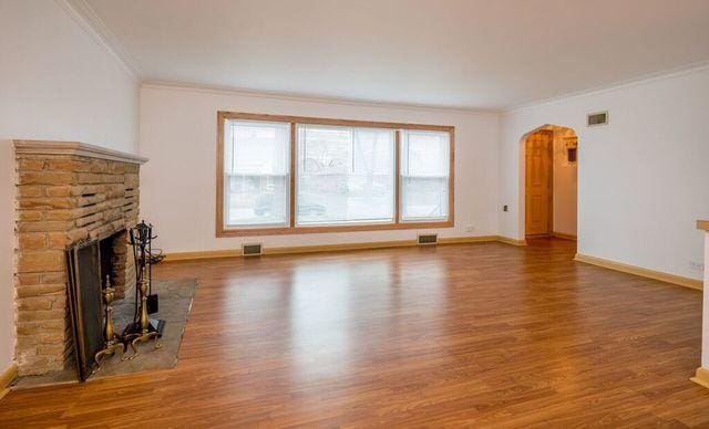 unfurnished living room featuring arched walkways, ornamental molding, and wood finished floors