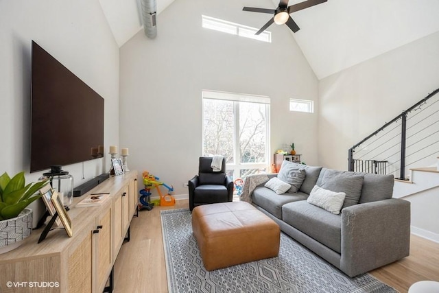 living area with light wood-style floors, baseboards, ceiling fan, and high vaulted ceiling