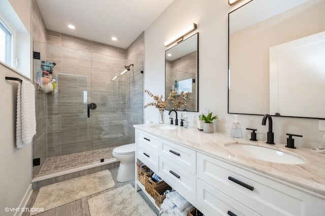 bathroom with double vanity, a sink, a stall shower, and toilet