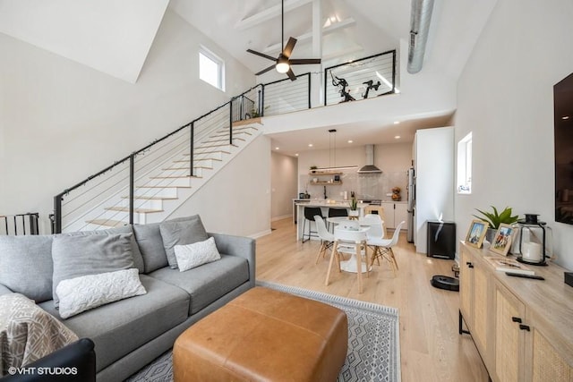 living area with stairs, baseboards, ceiling fan, a high ceiling, and light wood-style flooring