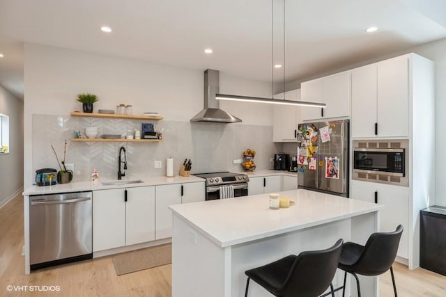 kitchen with wall chimney range hood, decorative backsplash, a sink, light wood finished floors, and stainless steel appliances