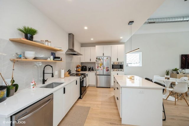 kitchen with open shelves, a kitchen island, wall chimney range hood, a sink, and appliances with stainless steel finishes