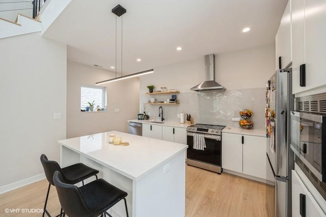 kitchen featuring a kitchen island, wall chimney range hood, tasteful backsplash, light wood finished floors, and stainless steel appliances