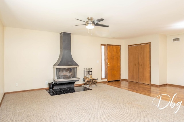 interior space featuring carpet, a wood stove, visible vents, baseboards, and ceiling fan