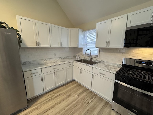 kitchen with a sink, stainless steel appliances, white cabinets, light wood-type flooring, and lofted ceiling