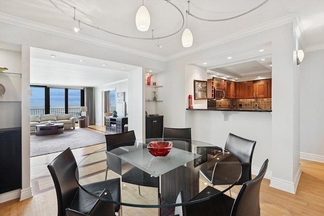 dining space featuring light wood-type flooring, ornamental molding, baseboards, and track lighting