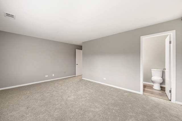 unfurnished bedroom with baseboards, ensuite bathroom, visible vents, and carpet