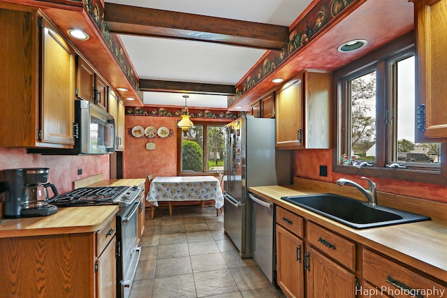 kitchen with appliances with stainless steel finishes, a sink, butcher block countertops, pendant lighting, and brown cabinetry