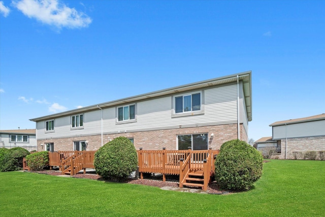 rear view of property with a yard, brick siding, and a wooden deck