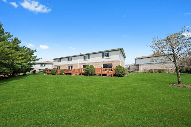rear view of property with a deck, brick siding, and a lawn
