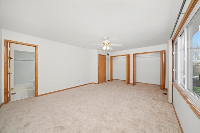unfurnished bedroom with baseboards, light carpet, two closets, a ceiling fan, and ensuite bath