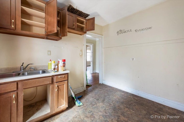 kitchen with open shelves, a sink, brown cabinetry, light countertops, and baseboards