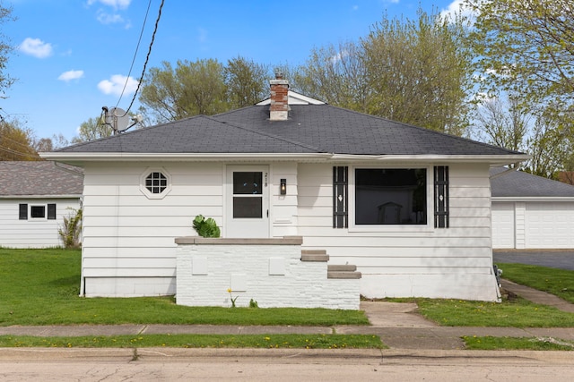 view of front of property with a chimney, a shingled roof, a front yard, and a garage