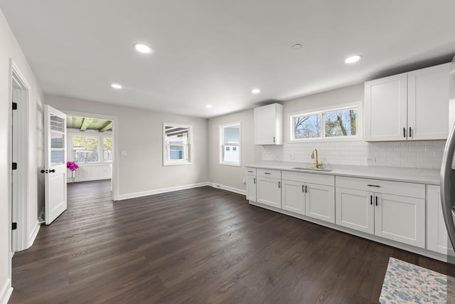 kitchen with backsplash, light countertops, a sink, white cabinets, and dark wood-style floors
