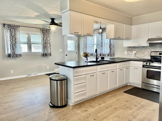 kitchen featuring dark countertops, a sink, under cabinet range hood, stainless steel gas range oven, and visible vents