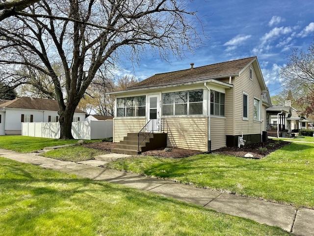 bungalow-style home with a front lawn, fence, and roof with shingles