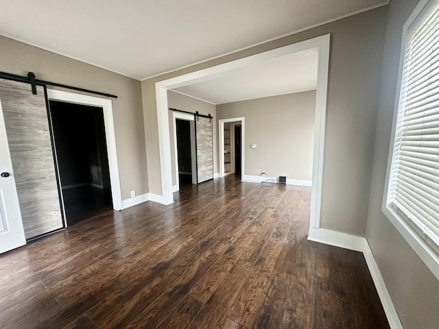unfurnished room featuring baseboards, dark wood-type flooring, and a barn door