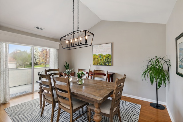 dining area featuring visible vents, vaulted ceiling, wood finished floors, baseboards, and an inviting chandelier