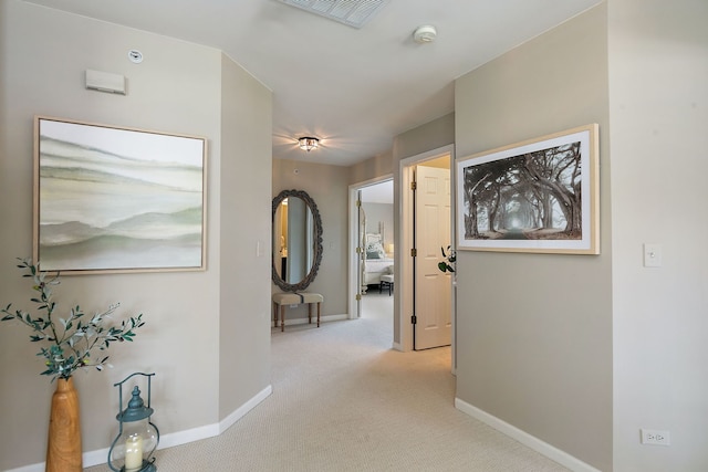 hall featuring baseboards, light carpet, and visible vents