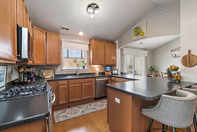 kitchen featuring appliances with stainless steel finishes, a sink, light wood-style flooring, a kitchen bar, and visible vents