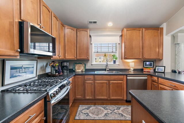 kitchen with visible vents, dark countertops, wood finished floors, a sink, and stainless steel appliances