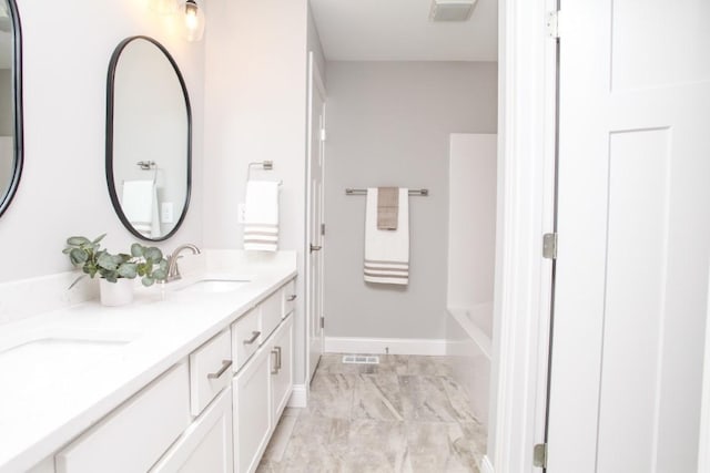 full bath featuring a sink, a bathtub, double vanity, baseboards, and visible vents