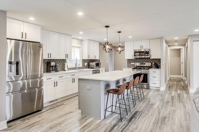 kitchen with decorative backsplash, stainless steel appliances, a kitchen island, light countertops, and a kitchen bar